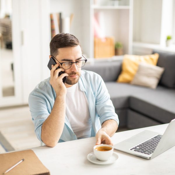 Serious businessman with smartphone going to have a cup of coffee while calling client or colleague by workplace