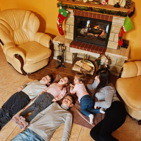 Happy young large family by a fireplace in warm living room on winter day. Mother with four kids at home.